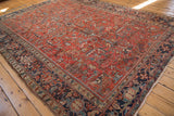 Vintage Heriz rug corner, brick red field, geometric floral patterns, navy border, fringe.