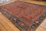 Vintage Heriz carpet corner revealing brick red field, navy geometric border, and low pile.