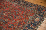 Corner of vintage Heriz carpet featuring brick red geometric field and navy blue border.