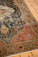Corner of antique Farahan Sarouk rug, showing worn scrolling floral design in dark blue, blush, ivory, and low pile.