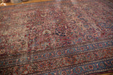 Ornate scrolling boteh and floral patterns on worn vintage Meshed carpet in red, navy, and beige.