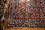 Corner of vintage Meshed rug, displaying worn blue curvilinear floral border design.