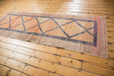 Vintage Oushak runner end with distressed geometric diamond pattern and textured raspberry border.