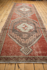 Distressed cherry red Oushak runner texture, showing narrow banded border and secured ends.