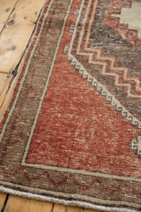 Distressed cherry red field of a vintage rug corner with geometric borders.