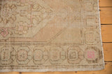 Distressed Oushak rug corner, featuring pale blush, beige abrashes, intact selvage, and fringe.