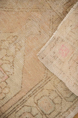 Distressed pile of vintage Oushak rug with beige and blush tones, revealing hand-knotted reverse with painted numbers.