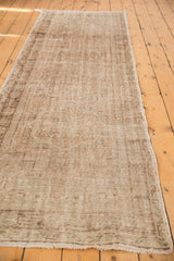 The distressed texture and short fringe of a vintage Oushak runner in muted beige and sand.