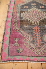 Distressed Oushak rug corner with raspberry pink border, mint triangles, and short fringe.