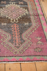 Distressed vintage Oushak rug corner featuring blush pink, charcoal, and green geometric motifs.