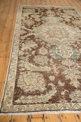 Distressed vintage Sparta rug corner, revealing worn pile, faded plum, and beige palmette motifs.