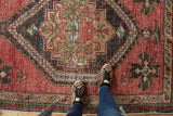 Distressed Oushak rug with worn cherry red field, dark medallion, and leopard print shoes from above.