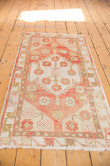 Distressed corner of a vintage Oushak runner, showing blush, ivory, gold floral motifs, and fringe.