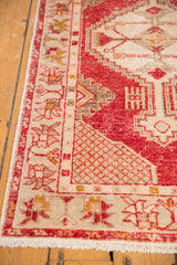 Vintage distressed Oushak rug corner, showing cherry red field, ivory geometric spandrel, and fringe.