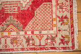Distressed vintage Oushak rug corner, revealing worn cherry red, ivory geometric patterns, and fringe.
