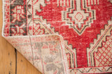 Distressed red and ivory Oushak rug corner, showing hand-knotted foundation and fringe.