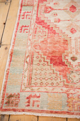 Distressed Oushak rug edge with textured pile, geometric motifs in blush red and pale aqua.