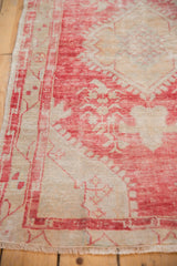 Distressed Oushak rug's faded raspberry field, revealing worn texture and ivory vine border.