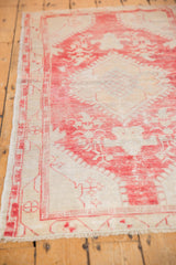 Distressed raspberry red and ivory Oushak rug corner, showing meandering vine border and secured fringe.