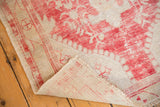 Vintage distressed Oushak rug corner with vibrant red pile, secured fringe, and visible foundation.