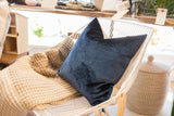 Luxe cobalt navy velvet throw pillow with a soft sheen, resting on a beige knitted blanket.