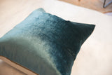 Close-up of the rich peacock teal velvet pillow, showing its varied texture and brass zipper.
