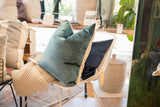 Peacock teal velvet throw pillow with natural linen trim on a white chair.