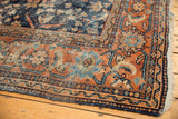 Vintage Mahal carpet corner showing terra cotta palmette border, navy field, and tattered edge.