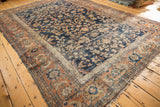 Vintage Mahal carpet detail: worn pile, tattered edge, navy floral field, rust palmette border.