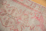 Distressed vintage Oushak rug with pale blush scrolling patterns, even wear, and a beige ground.