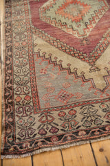 Fringed corner of distressed Oushak runner, showing geometric border and aubergine floral motifs.