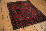 Angled view of vintage Lilihan rug with raspberry field, navy floral palmettes, meandering border.