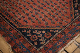 Antique Kurdish Hamadan rug corner, madder red field, navy floral spandrel, and worn edge.