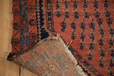 Antique Kurdish Hamadan rug's folded corner, showing madder red pile, navy patterns, and tattered fringe.