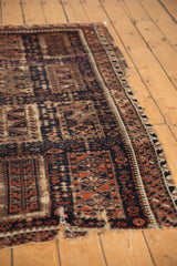 Antique Belouch rug fragment showing visible holes, tattered edges, and dark navy geometric patterns.