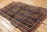 Antique Belouch rug with navy and madder root red geometric motifs and tattered perimeter.