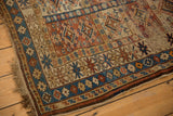 Tattered end and worn pile showcasing brick red geometric motifs on an antique Caucasian rug.