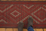 Antique Verneh rug runner, geometric diamond pattern in brick red, ivory, and blue, with suede boots.