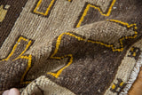 Distressed wool pile shows chocolate, ivory, and saffron yellow geometric motifs and fringe.
