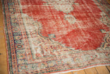 Distressed Oushak rug corner, wear revealing cherry red field and antique ivory spandrel design.