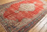 Distressed vintage Oushak rug corner, cherry red field, visible foundation, and intricate blue-green border.