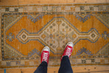Vintage Oushak rug runner featuring a distressed saffron orange field with geometric medallion.