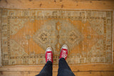 Distressed vintage Oushak runner, highlighting its textured pile, tangerine, ivory, and bronze medallion.