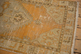 Distressed Oushak rug corner: worn tangerine field, geometric bronze border, visible foundation.