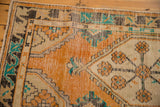 Distressed Oushak rug runner corner with tangerine orange, ivory, turquoise, and charcoal, showing vine and hook motifs.