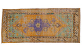 Distressed vintage Oushak runner with faded saffron, lavender, and mint diamond medallion.