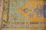 Distressed Turkish Oushak rug corner showing saffron yellow, mint green, and worn geometric patterns.