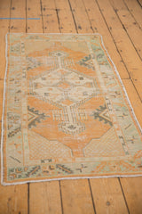 Distressed Oushak rug corner showing wear, pale tangerine and mint green patterns.