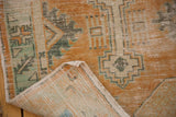 Distressed orange and green Oushak rug, showing wear, hand knotted foundation, and selvage.