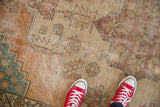 Distressed vintage Oushak rug with pale terra cotta, beige, teal geometric patterns, visible foundation.